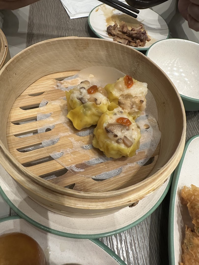 A bamboo steamer basket filled with delicious dim sum, likely siew mai, on a table.