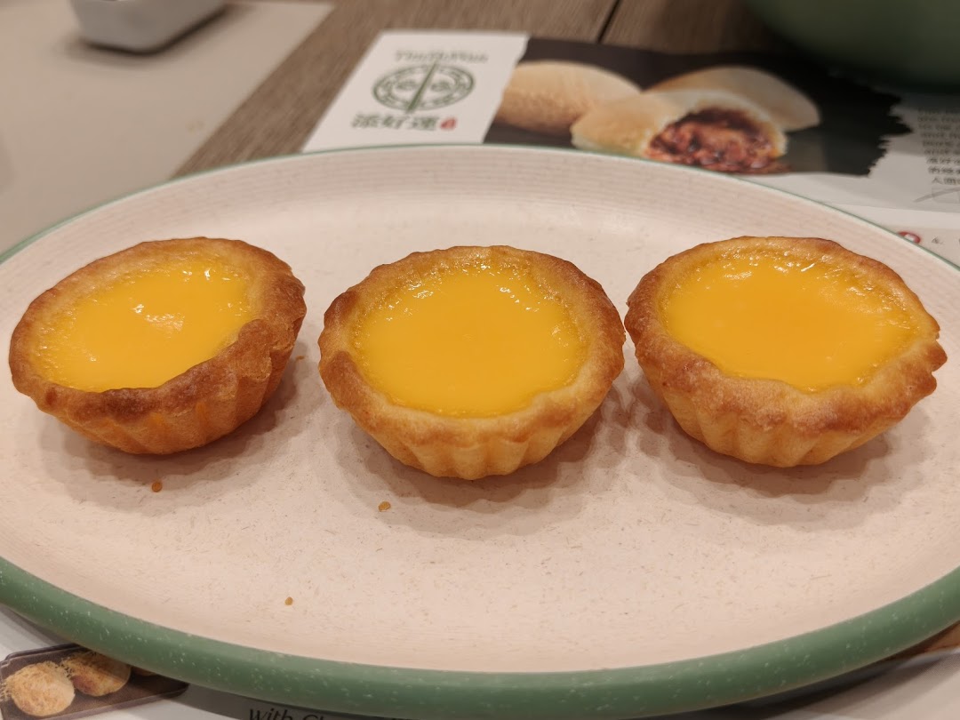 Three golden egg tarts on a plate, with a Tim Ho Wan menu visible in the background.