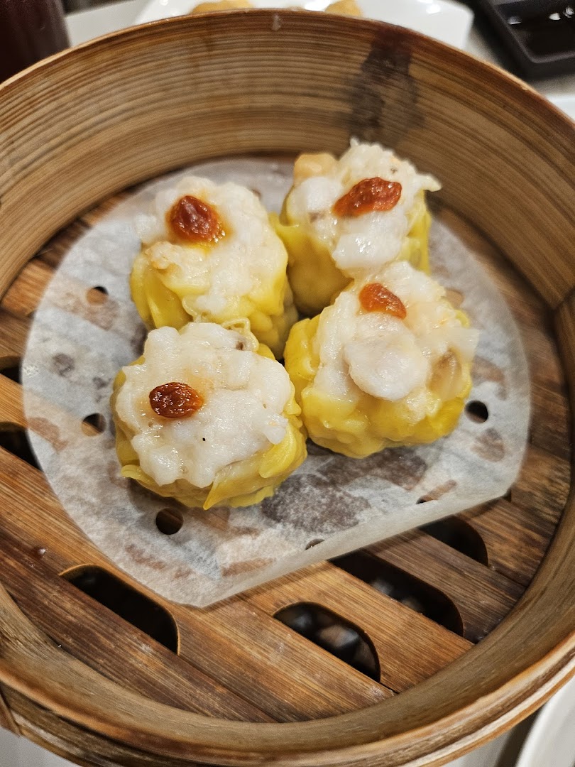 Close-up of four delicious dim sum (siew mai) in a traditional bamboo steamer, ready to be enjoyed.