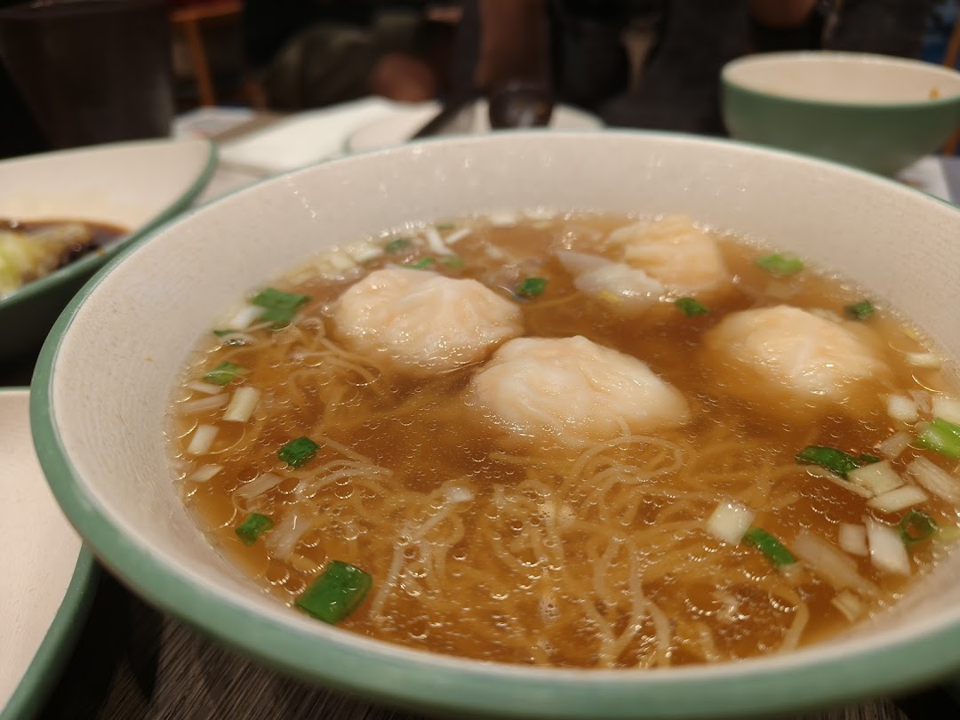 A close-up of a steaming bowl of shrimp wonton noodle soup, garnished with fresh green onions.
