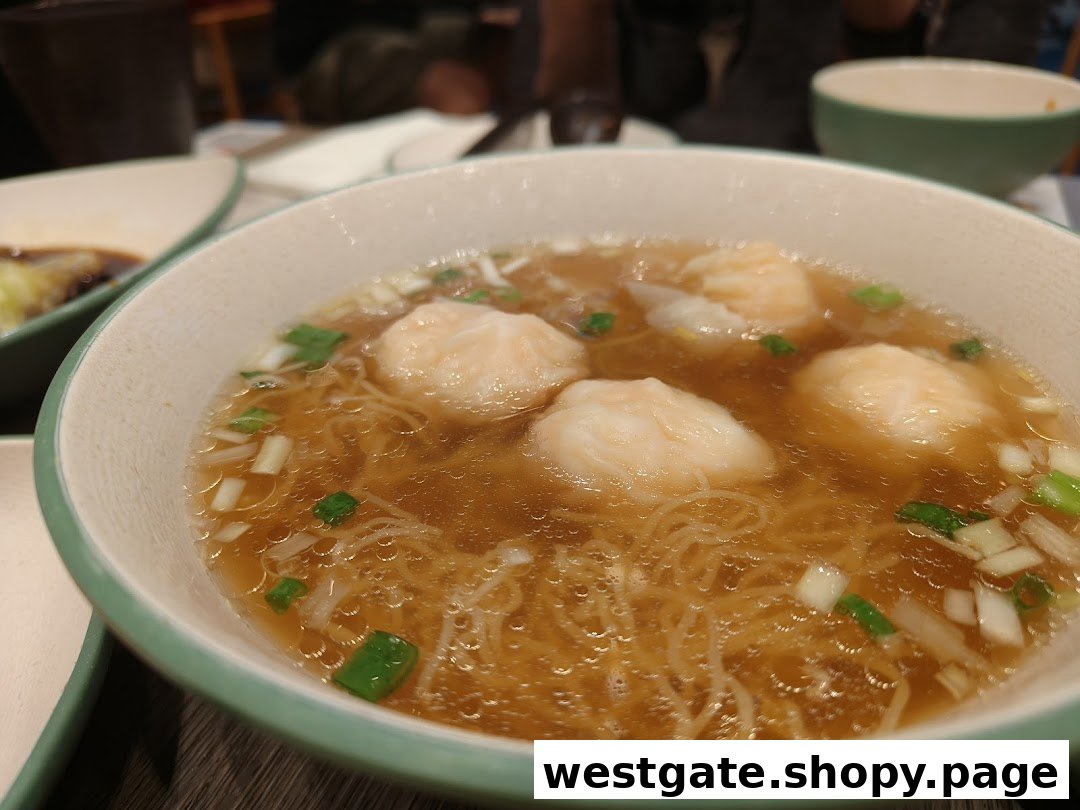 A close-up of a steaming bowl of shrimp wonton noodle soup, garnished with fresh green onions.