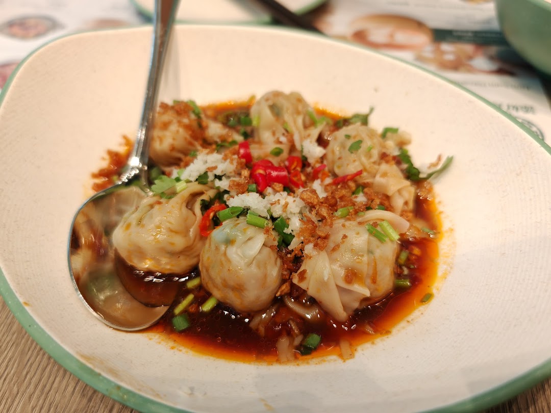 A close-up of savory dumplings or wontons in a rich sauce, garnished with chili, garlic, and spring onions.