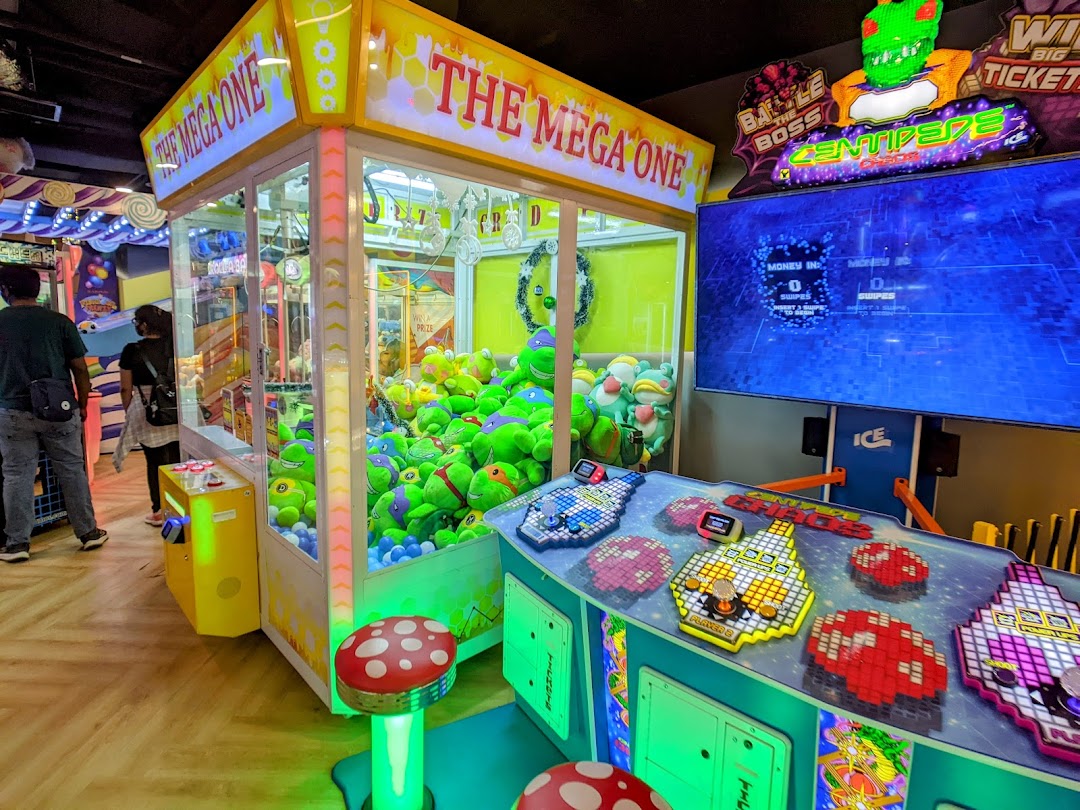 Vibrant arcade interior featuring a large claw machine filled with plush toys and an interactive video game.
