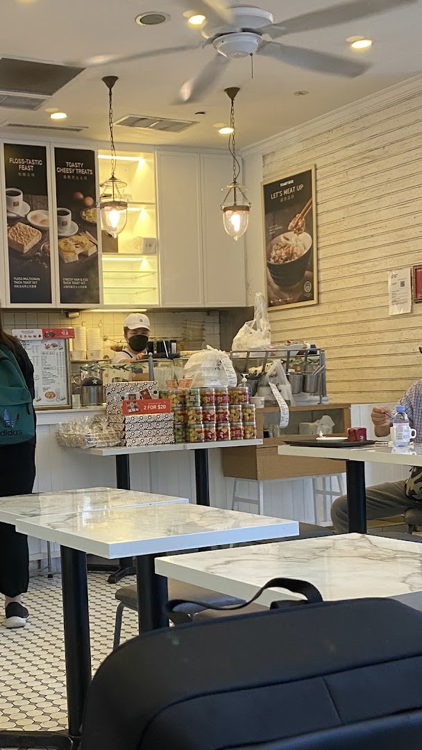 An interior view of Toast Box, showing the counter, staff, marble tables, and promotional posters.
