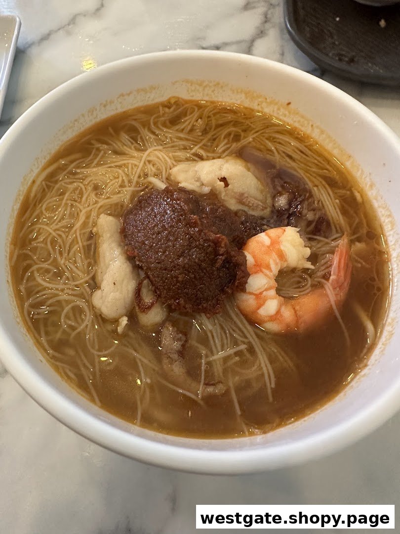 A close-up of a delicious bowl of noodles with shrimp, fish cake, and a rich sauce from Toast Box.