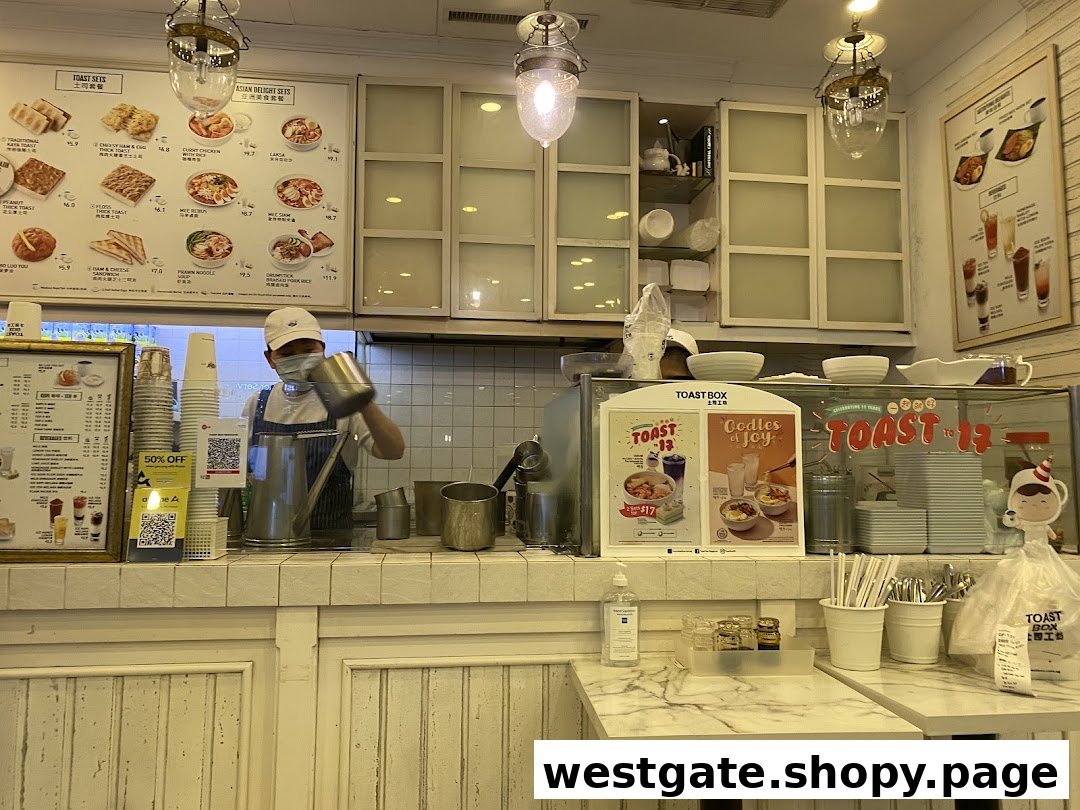 A staff member prepares drinks behind the counter at Toast Box, with menu boards and promotional displays visible.
