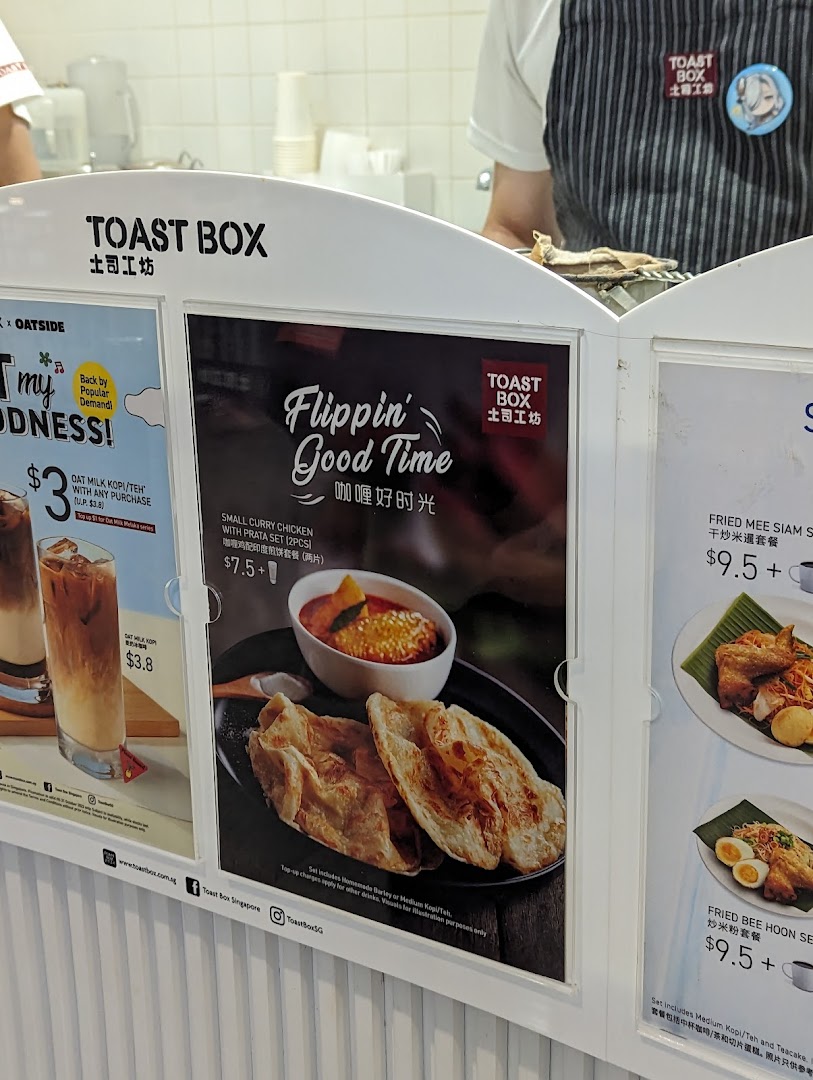 A close-up of Toast Box's menu display featuring curry chicken prata, fried noodles, and oat milk drinks.