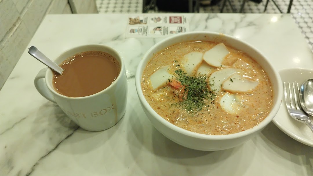 A bowl of laksa and a cup of coffee on a marble table at Toast Box.