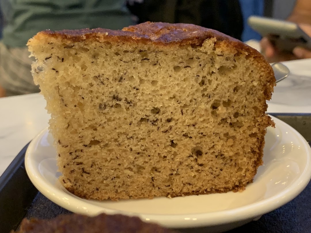 A close-up of a delicious slice of banana bread or cake served on a white plate.