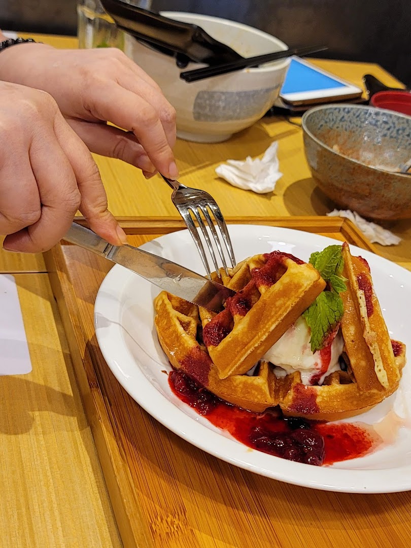 A person cuts into delicious waffles topped with ice cream, berry sauce, and mint at Tokyo Shokudo Westgate.