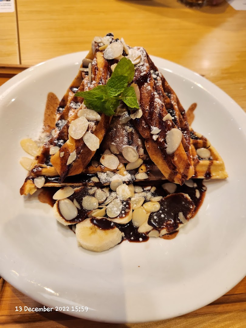 Waffles with chocolate, almonds, powdered sugar, mint, and banana slices on a white plate.
