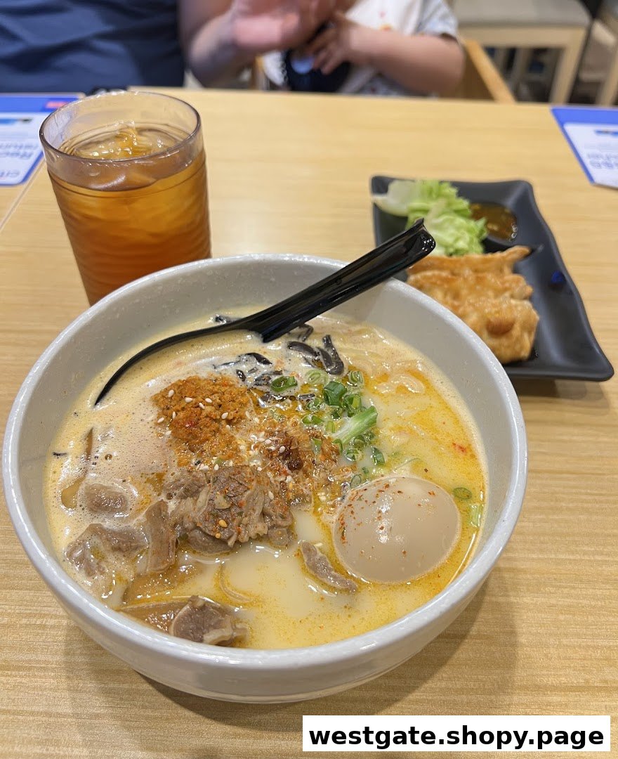 A close-up of a creamy ramen bowl with meat and egg, served with gyoza and iced tea.