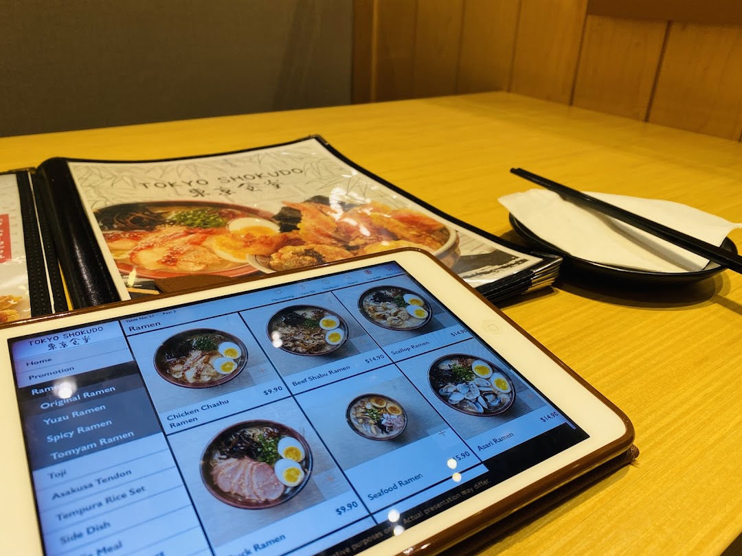 A table setting at Tokyo Shokudo featuring a physical menu and a tablet displaying various ramen dishes.