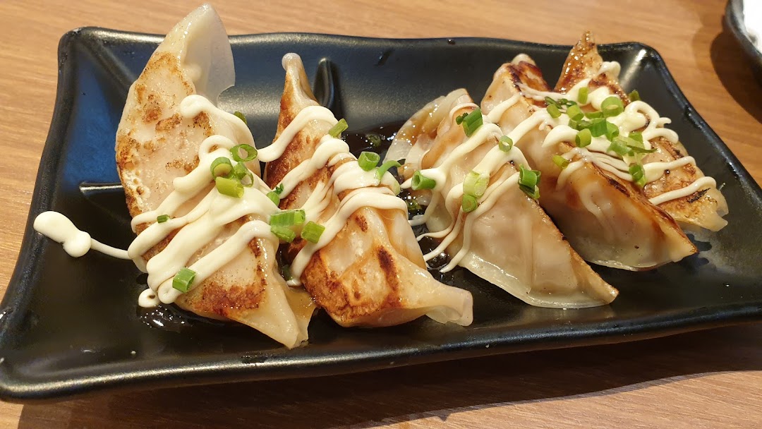A plate of pan-fried gyoza topped with mayonnaise and chopped spring onions.