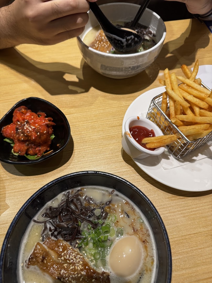 A table with two bowls of ramen, a side of fries, and a spicy appetizer.