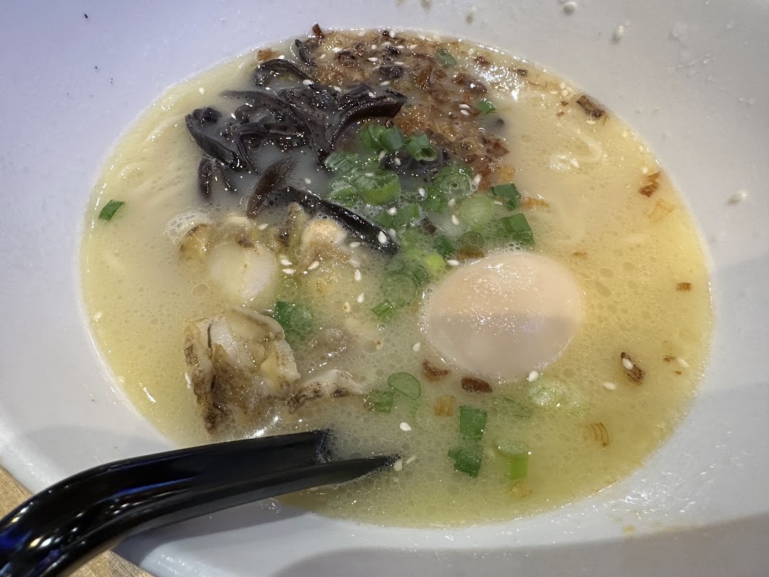 A close-up of a creamy ramen bowl with wood ear mushrooms, green onions, sesame seeds, and a soft-boiled egg.
