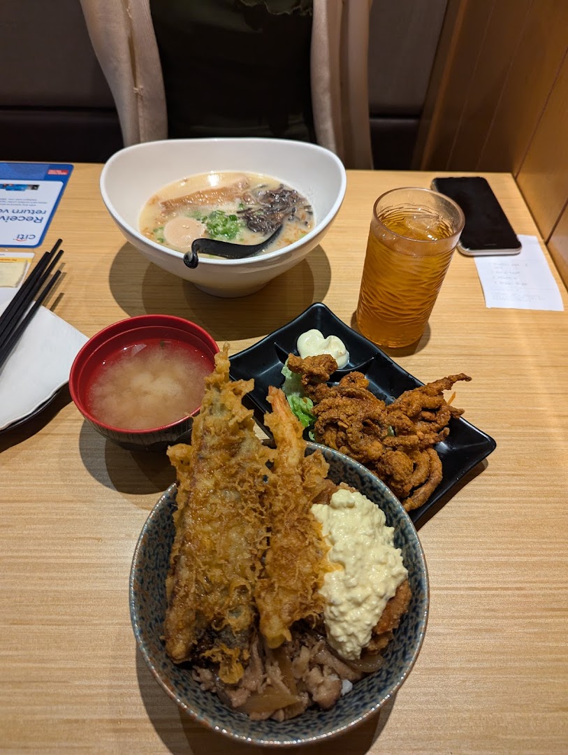 A delicious Japanese meal featuring ramen, tempura donburi, miso soup, and fried soft-shell crab on a wooden table.