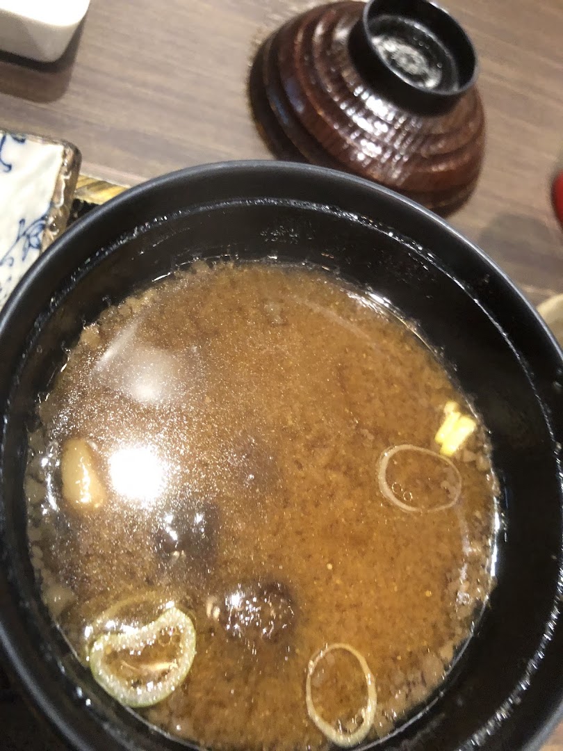 A close-up view of a steaming bowl of miso soup with scallions and other ingredients.