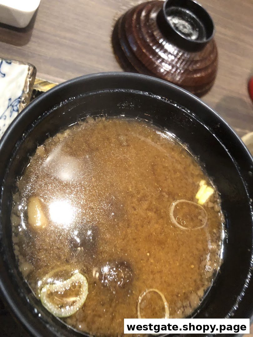 A close-up view of a steaming bowl of miso soup with scallions and other ingredients.