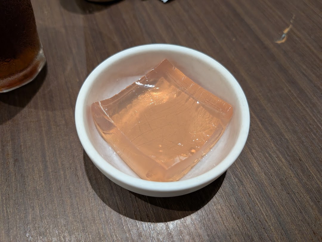 A small white bowl holds a clear, light orange jelly dessert on a wooden table.