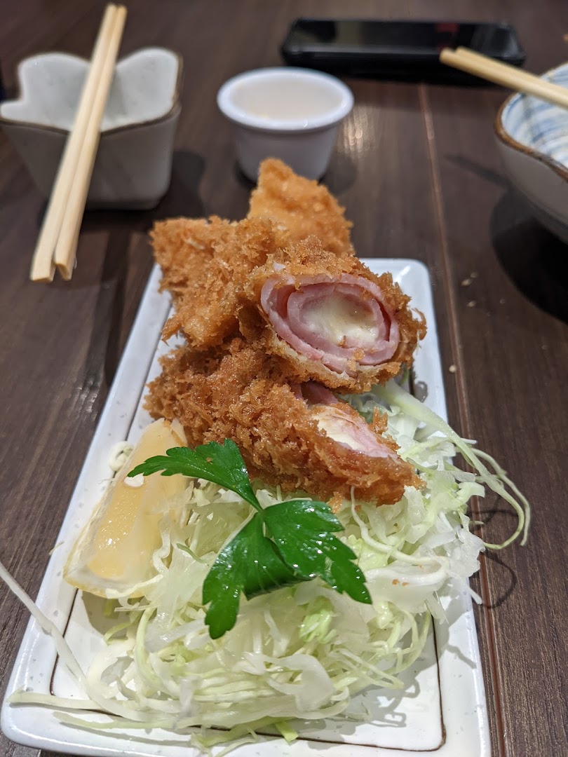 A plate of crispy tonkatsu with ham and melted cheese, served with shredded cabbage and lemon.