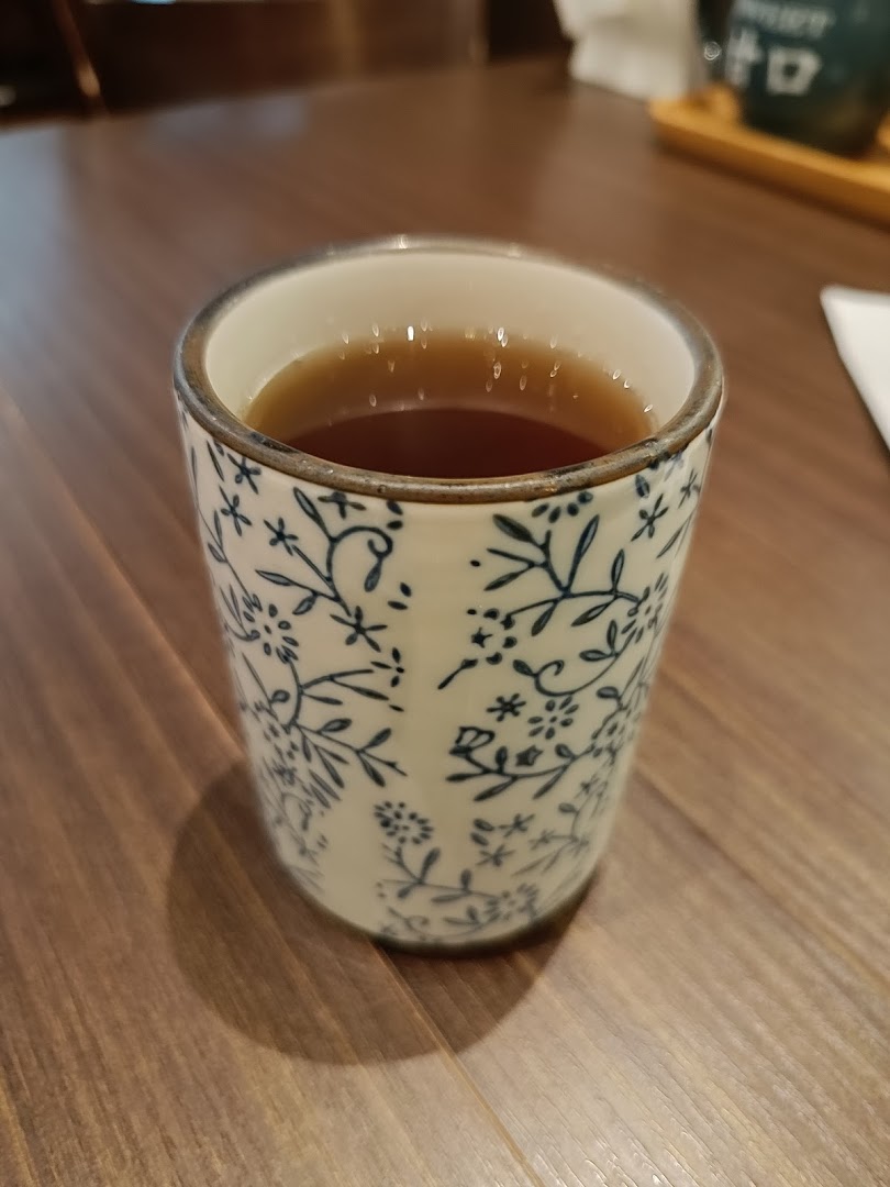 A decorative ceramic cup filled with a warm beverage, likely tea, on a wooden table.