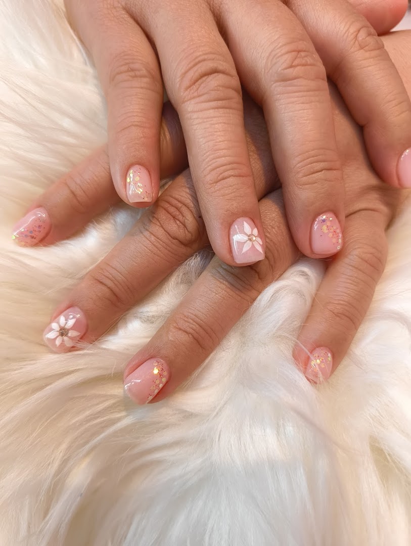 A close-up of hands displaying a delicate pink manicure with glitter and white floral nail art.