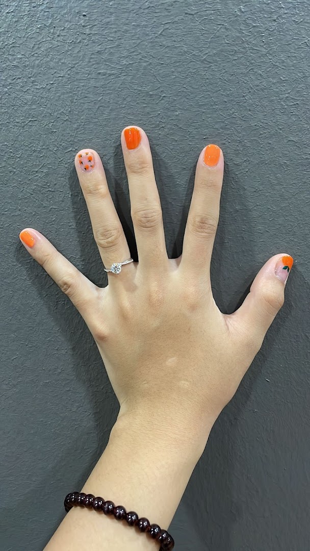 A hand showcasing vibrant orange nail polish with delicate designs and a sparkling ring.