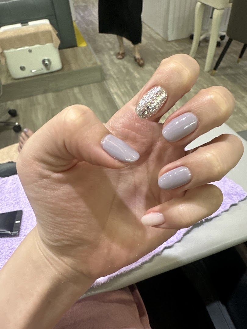 A close-up of a hand showcasing a fresh manicure with glitter and solid light-colored nails in a salon setting.