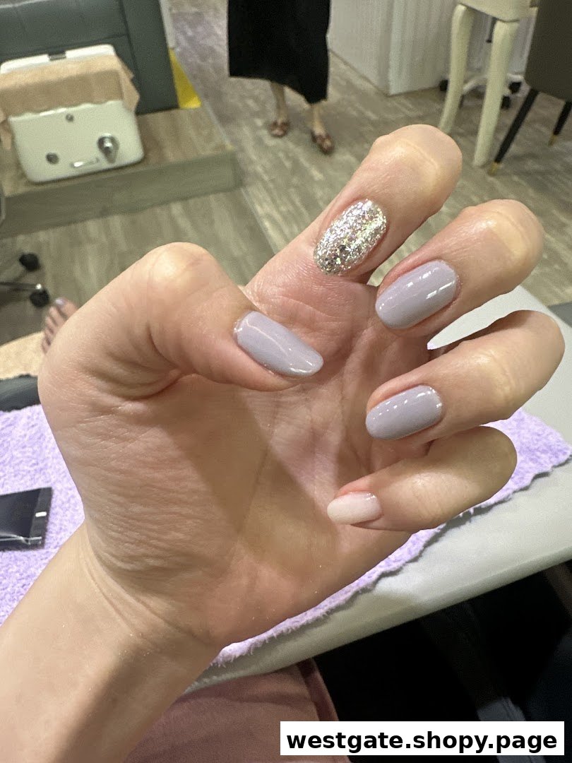 A close-up of a hand showcasing a fresh manicure with glitter and solid light-colored nails in a salon setting.