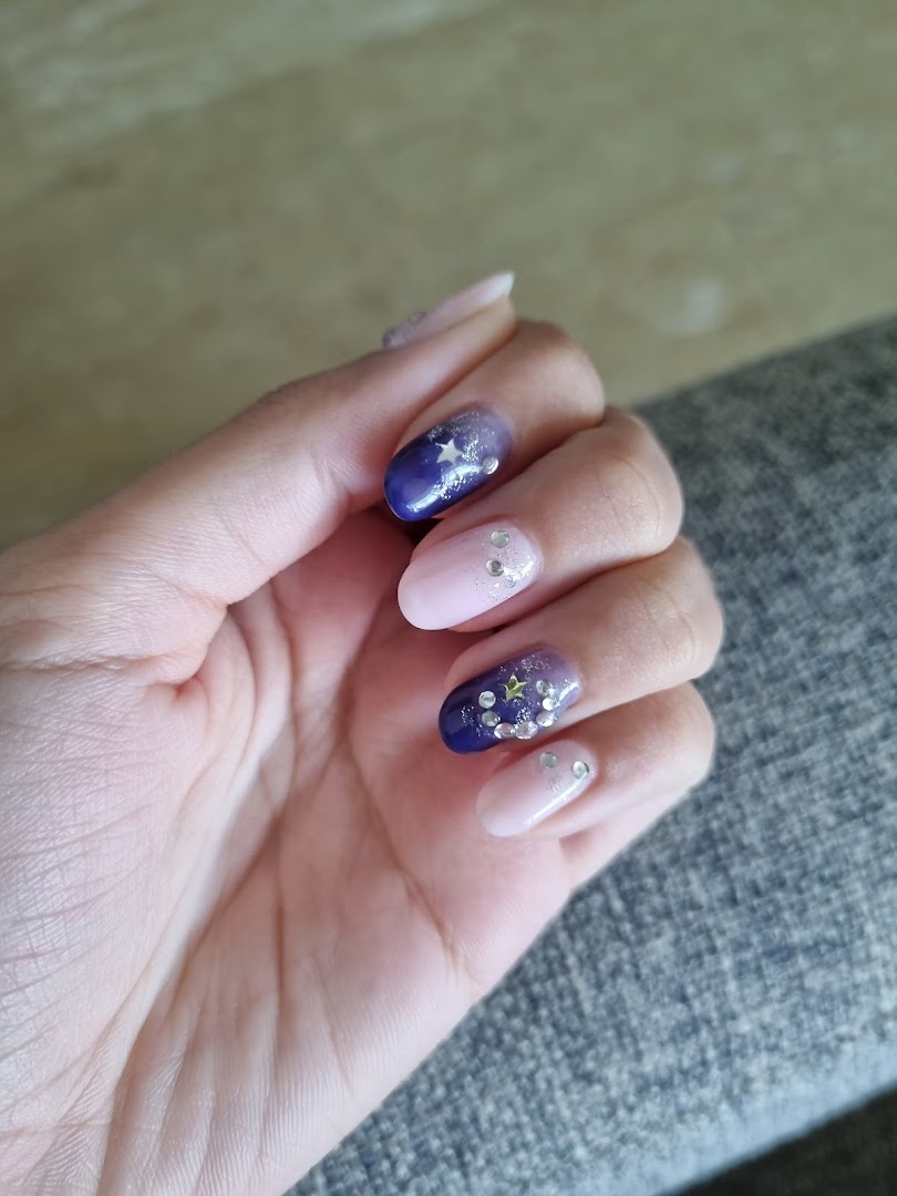 A hand showcasing beautifully designed nails with purple, pink, glitter, and star accents.