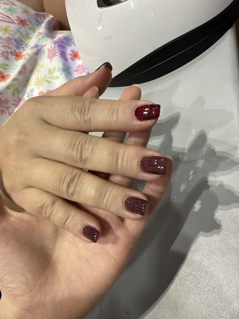 A hand showcasing freshly applied glittery red nail polish, likely drying under a UV lamp.