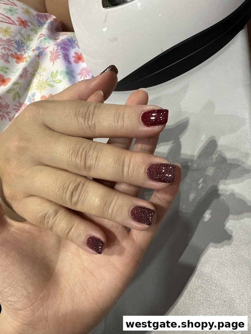 A hand showcasing freshly applied glittery red nail polish, likely drying under a UV lamp.