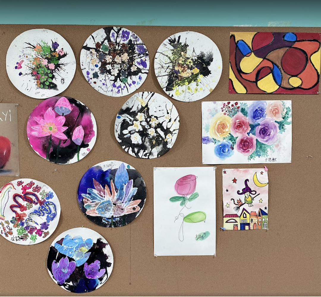 A vibrant display of diverse student artworks, including paintings and mixed media pieces, on a brown corkboard.