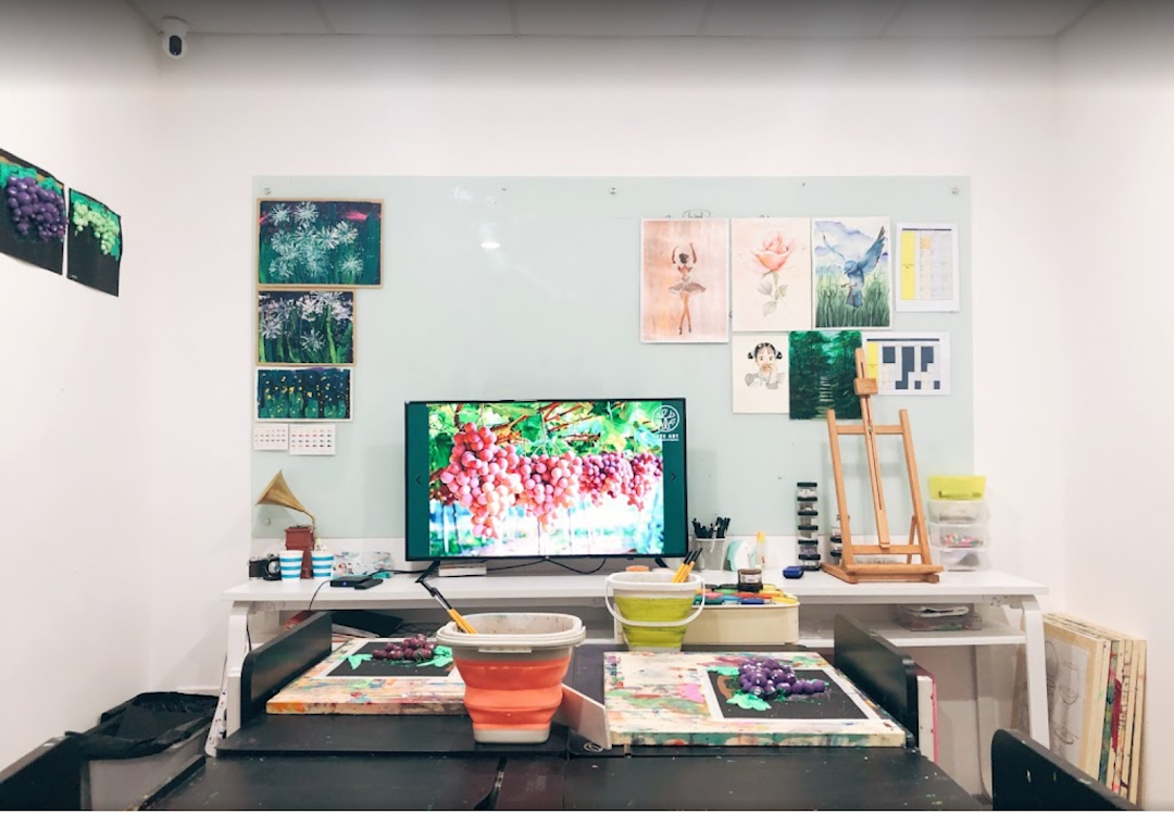 An art studio workspace featuring art supplies, student artworks, a large screen, and creative projects in progress.