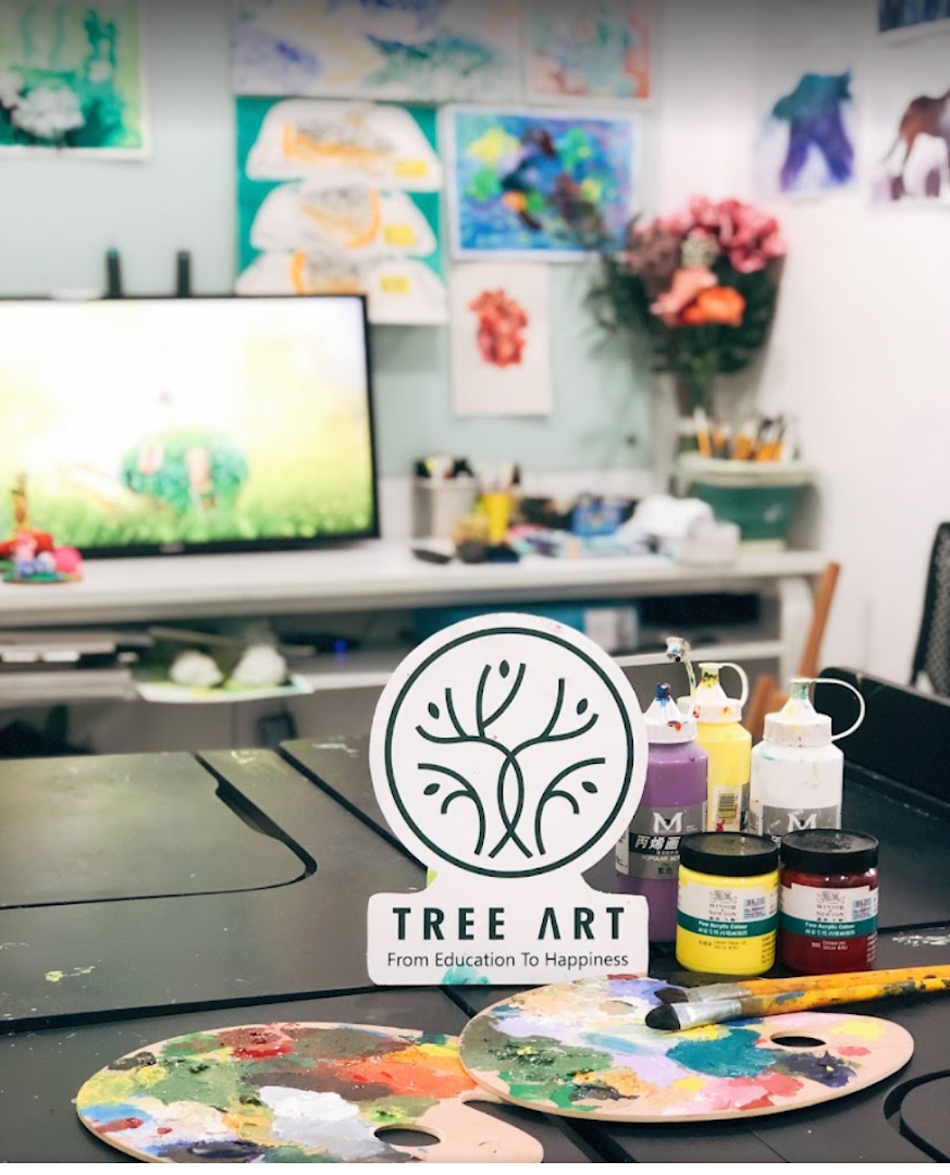 An art studio interior featuring paint palettes, brushes, paints, and student artworks, with the 'Tree Art' logo prominently displayed.