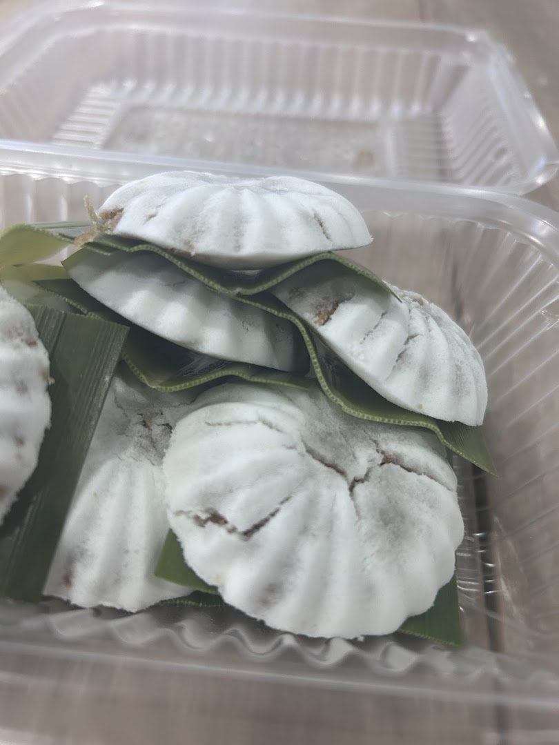 Close-up of several white, round coconut cakes with green leaves in a clear plastic container.