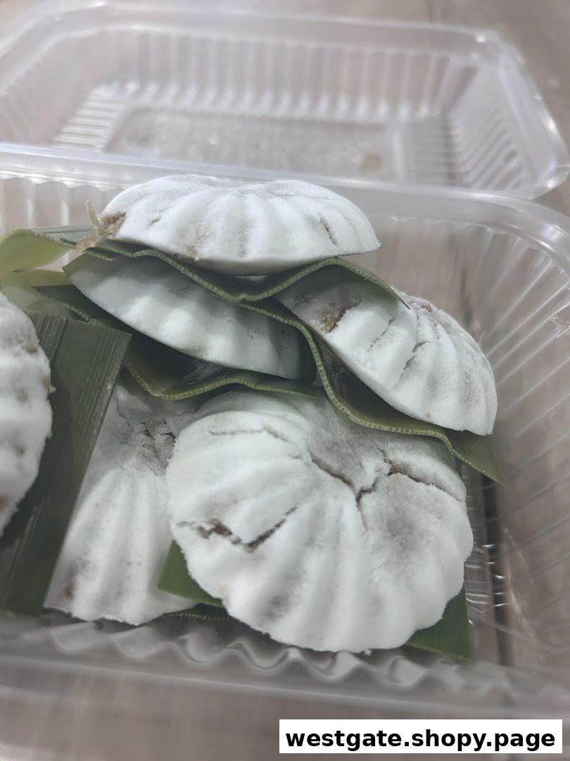 Close-up of several white, round coconut cakes with green leaves in a clear plastic container.