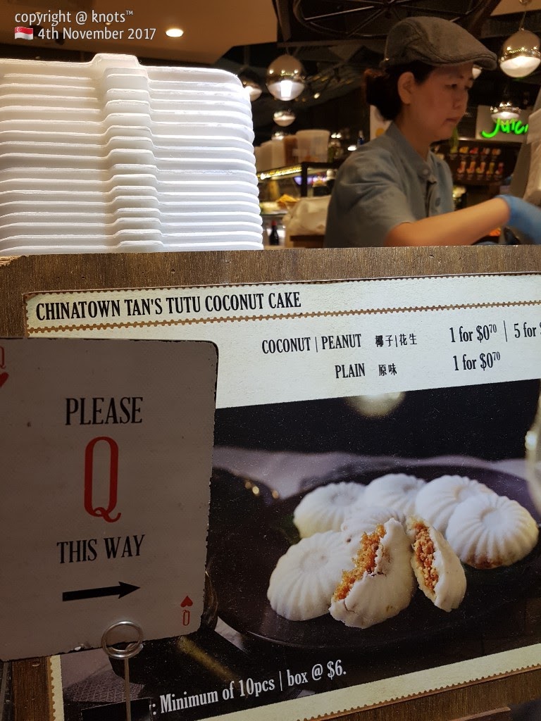 A counter display featuring traditional Tutu Coconut Cakes, pricing, and a staff member.