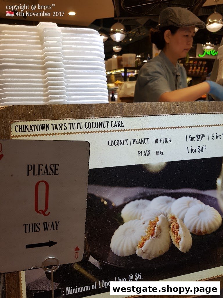A counter display featuring traditional Tutu Coconut Cakes, pricing, and a staff member.