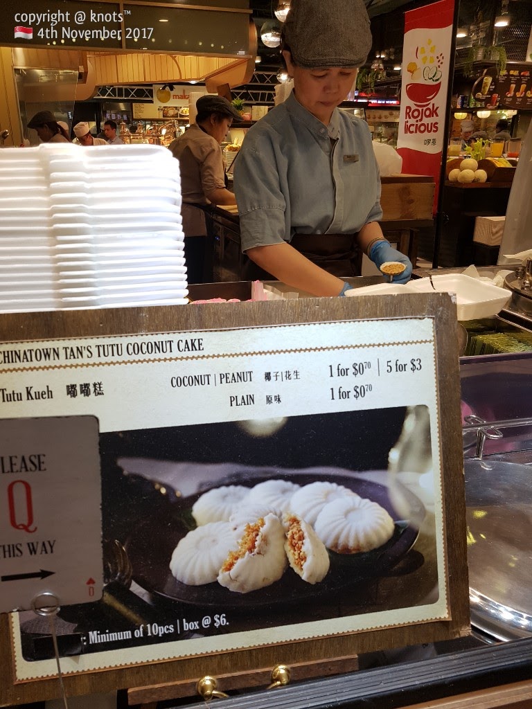 A vendor prepares traditional Tutu Kueh, with a clear menu board displaying prices and options.