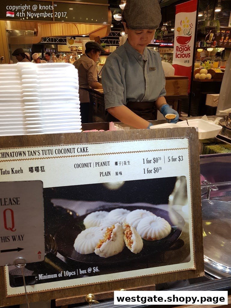 A vendor prepares traditional Tutu Kueh, with a clear menu board displaying prices and options.