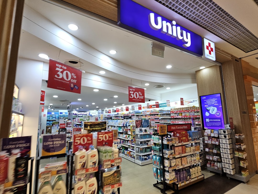 The brightly lit entrance of Unity pharmacy, showcasing various health, beauty, and wellness products with ongoing promotions.