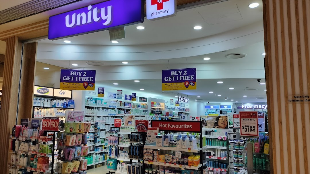 The entrance of Unity Pharmacy, showcasing health and beauty products, promotions, and operating hours.