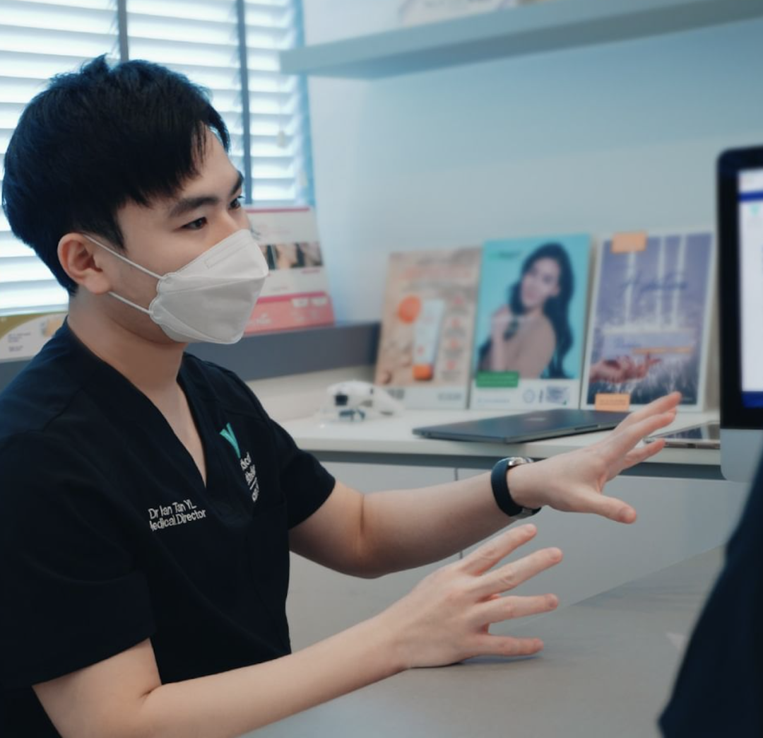 A masked medical professional consults with a client in a modern aesthetic clinic setting.