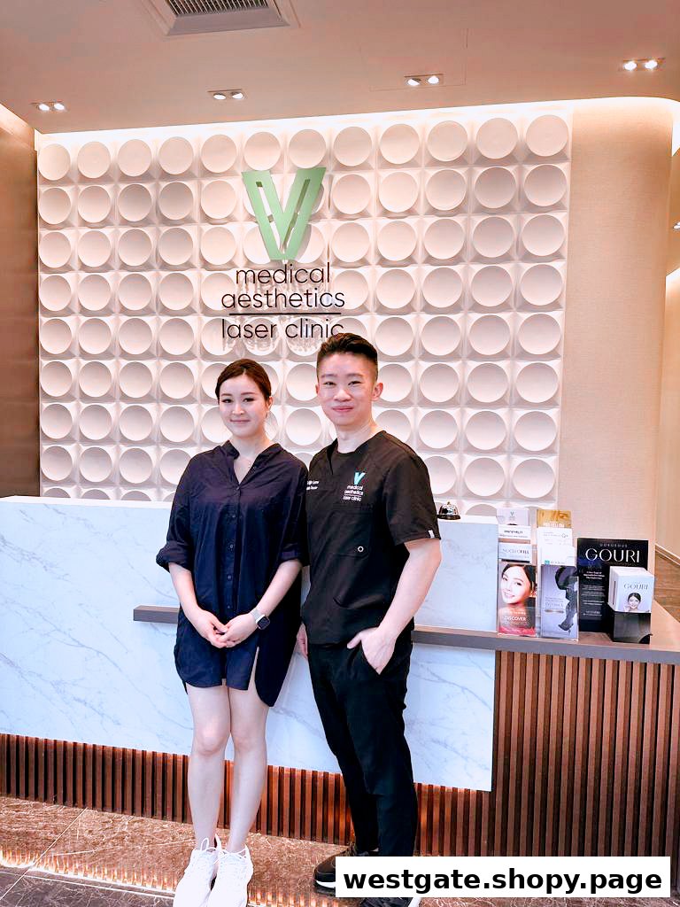 Two individuals stand at the reception of V Medical Aesthetics Laser Clinic, featuring its logo and modern decor.