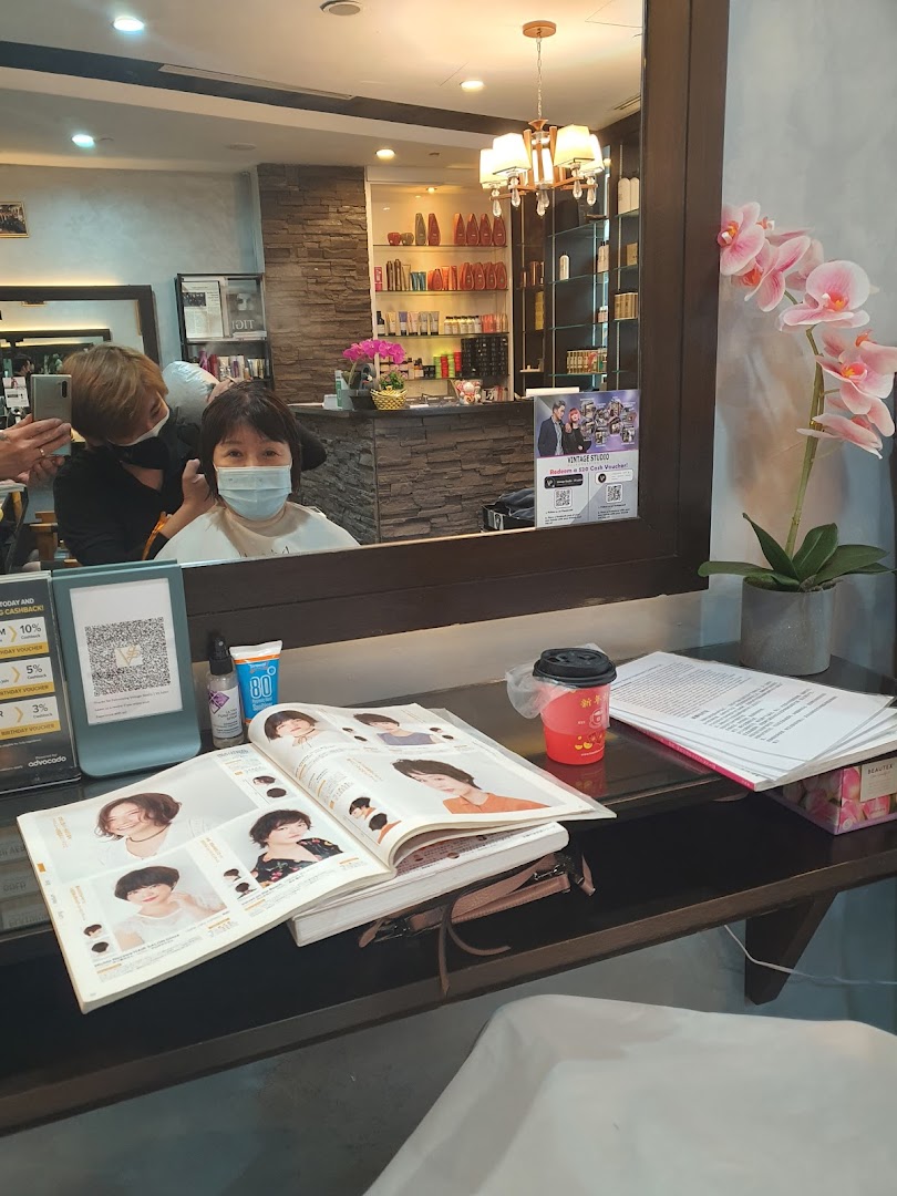 A customer receives a haircut at Vintage Studio VS Salon, with a style book and products visible.