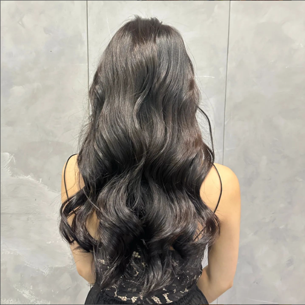 A person's back showcasing long, dark, voluminous wavy hair, likely a salon styling result.