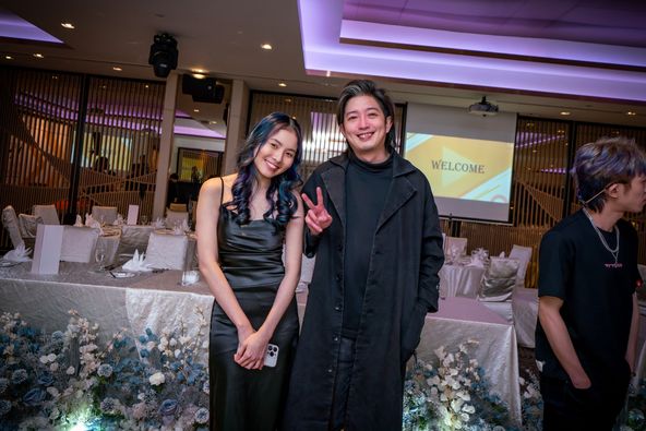 Two stylish individuals, likely salon staff, pose in an elegant event space with a 'WELCOME' screen.
