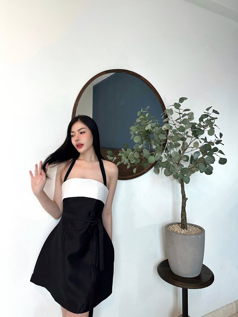 A person models a black and white dress in a minimalist interior with a mirror and plant.